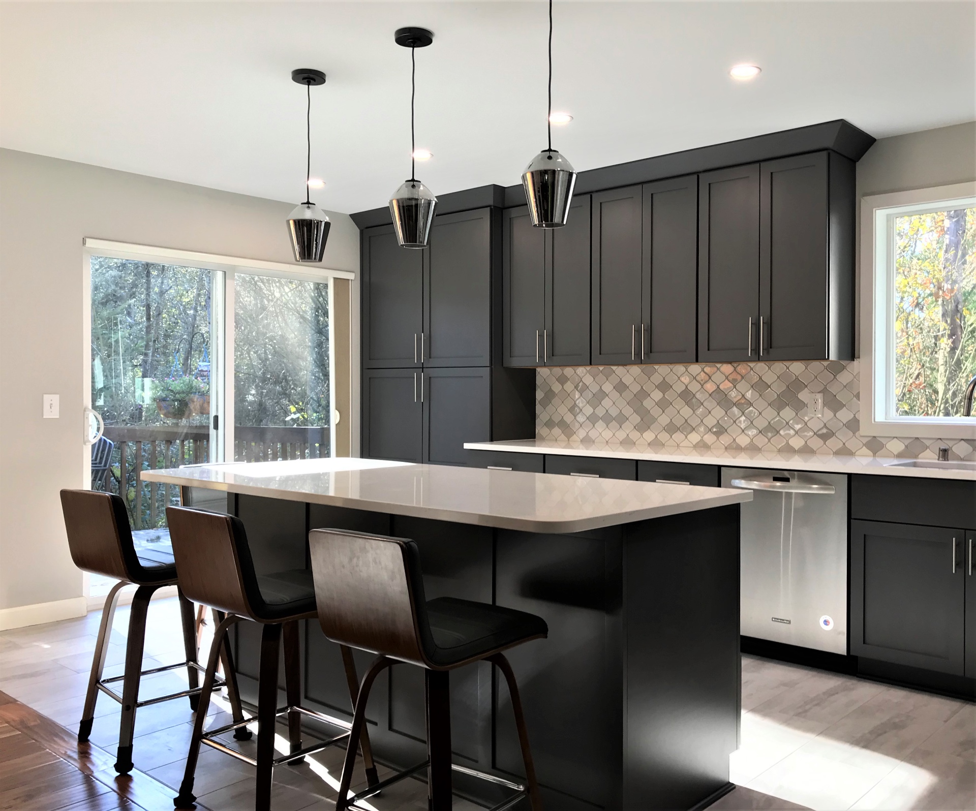 Charcoal kitchen island with three smoked-glass pendants opening to deck and backyard