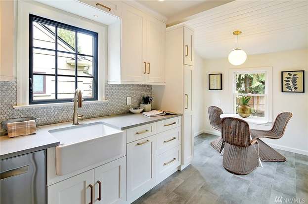 Bright white Shaker kitchen with farmhouse sink, brass hardware, and breakfast nook with woven chairs and globe pendant