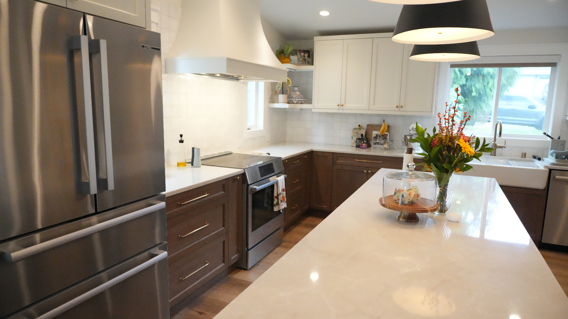 Walnut base cabinetry, induction range, and quartz island with pendant lighting