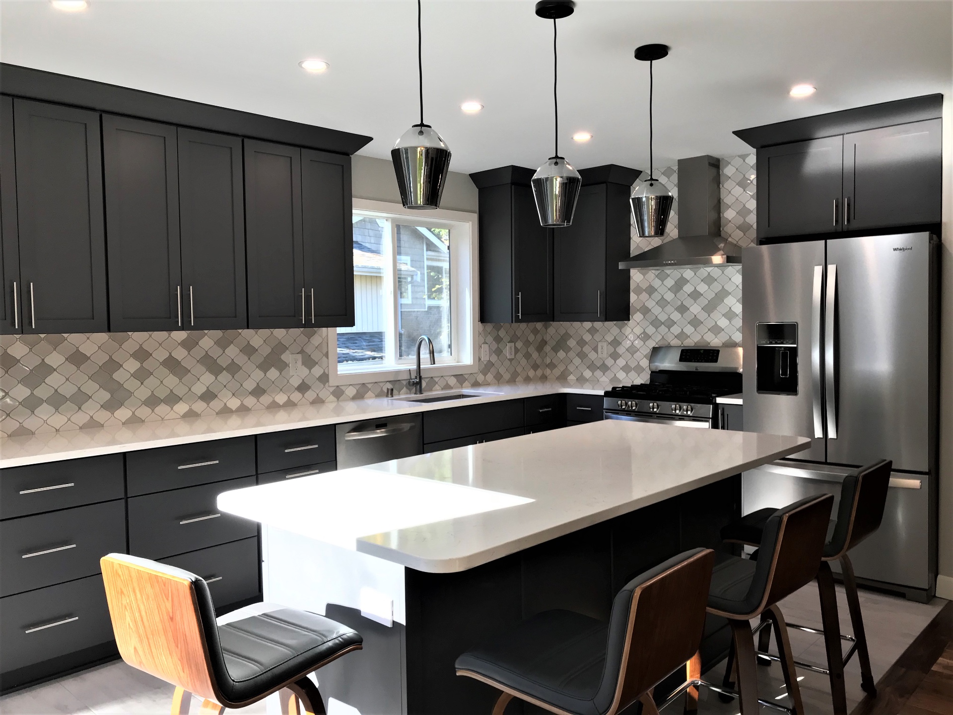 Wide view of charcoal kitchen with island seating, stainless appliances, and chimney hood