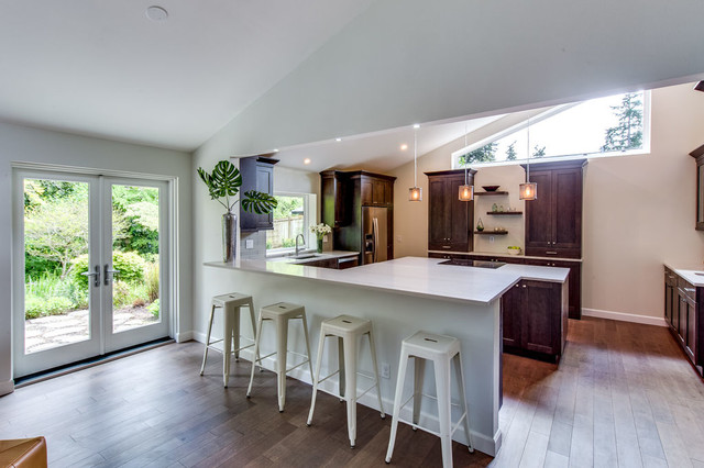 Open chef's kitchen with quartz waterfall island, walnut cabinetry, and vaulted ceiling opening to garden patio