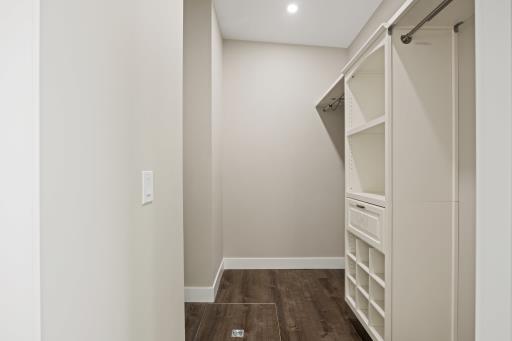 Walk-in closet with custom built-in shelving, drawers, hanging rods, and hardwood flooring