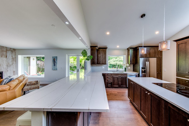 Long quartz island with marble veining looking through to living room and reclaimed-wood fireplace wall
