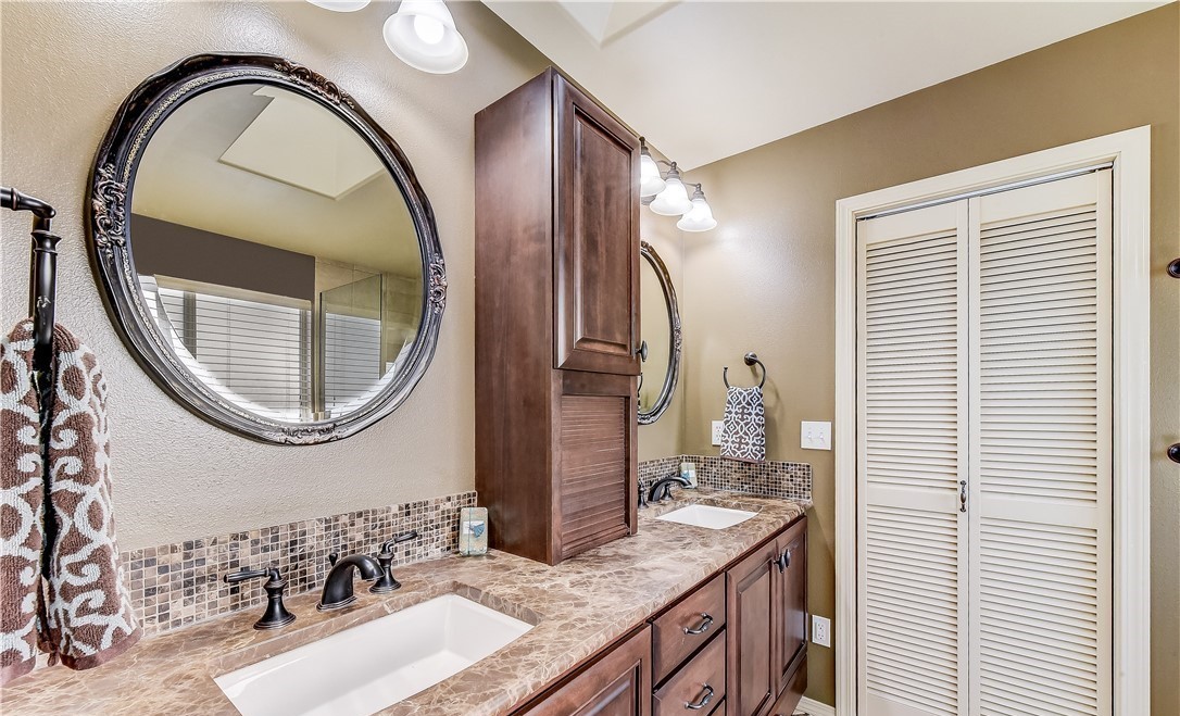 Traditional dual-vanity bathroom with oil-rubbed bronze fixtures, oval framed mirrors, mosaic tile backsplash, and warm wood cabinetry