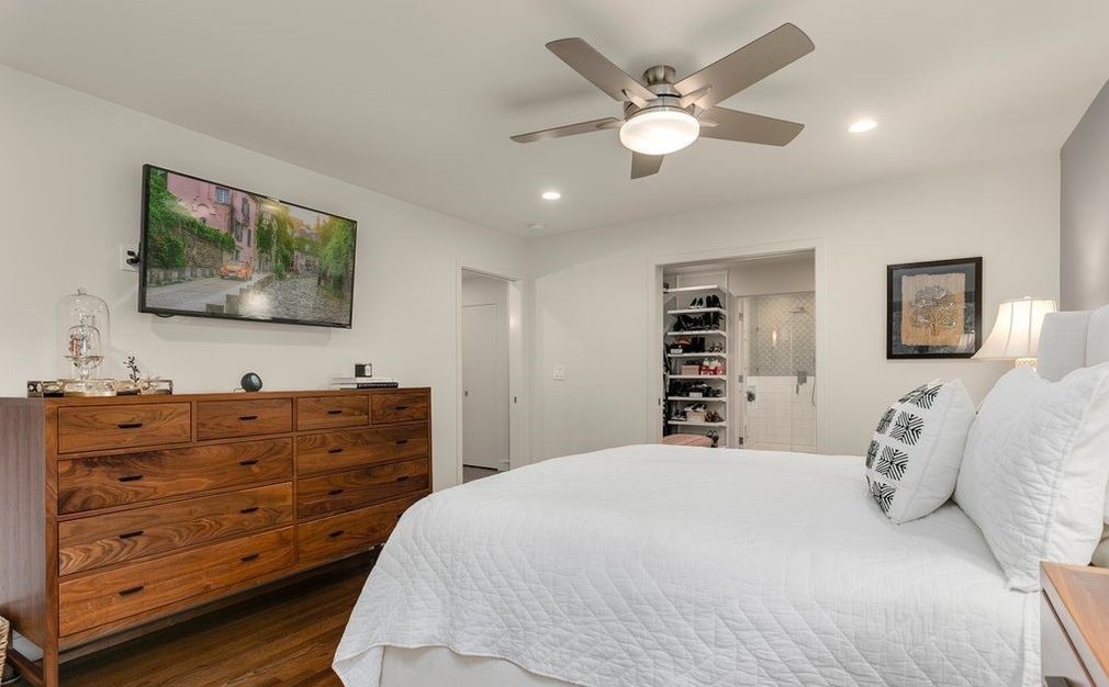 Primary bedroom with walnut dresser, mounted TV, and view into walk-in closet and bath