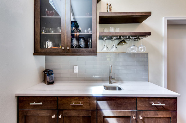 Custom wet bar with walnut cabinetry, glass-front uppers, floating shelves, and stainless bar sink