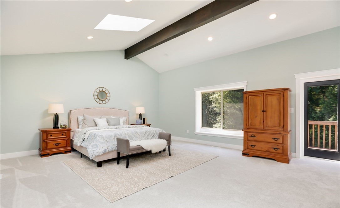 Primary suite with vaulted ceiling, hardwood floors, and large windows